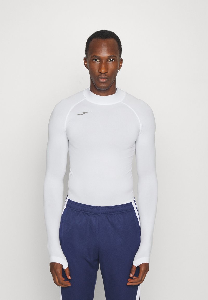 White long-sleeve athletic shirt with ribbed texture, featuring a high neckline and logo detail. Paired with navy pants with side stripes.