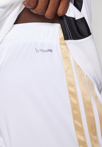 White athletic shorts feature a black accent and gold side stripes. The waistband is elastic, and "CLIMACOOL" branding is visible.