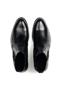 Scarpe slip-on in pelle nera con una finitura liscia e lucida, pannelli elastici laterali, punta arrotondata e dettagli di cucitura minimi.