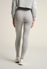 Grå, åtsittande leggings i mjukt, stretchigt tyg med en slät yta och utan synliga mönster, parat med vita träningsskor.