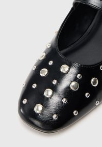 Black synthetic leather shoe with a square toe design, featuring silver studs of varying sizes across the upper surface for added texture.