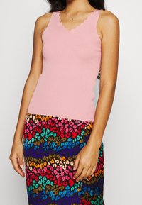 Top rosa chiaro a coste con scollo smerlato, abbinato a una gonna multicolore con stampa leopardata dai toni audaci e vivaci.