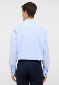 Himmelblaues Langarmhemd mit klassischem Kragen, ausgestattet mit dunklen Knöpfen an den Manschetten, kombiniert mit dunklen Hosen und glatter Textur.