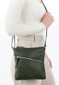 Grüne Leder-Crossbody-Tasche mit strukturiertem Oberflächenmaterial, einer Vorderreißverschlusstasche und einem verstellbaren Schultergurt. Kompakte, rechteckige Form.