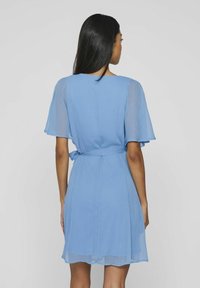 Svetlomodré šaty s krátkymi rozšírenými rukávmi a viazaným pásom, vyrobené z jemnej textúrovanej látky s voľným strihom.