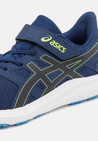 Chaussure de sport marine avec tige en mesh, accents verts et logo noir. Dotée d'une sangle Velcro et d'une semelle blanche avec semelle bleue.