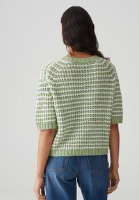 Top en tricot vert à manches courtes avec des rayures texturées en vert clair et foncé, terminé par un col et un ourlet côtelés. Coupe décontractée.