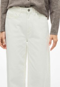 Pantalones anchos blancos de mezclilla, con cierre de botón en la parte delantera, bolsillos laterales y un corte recto que cae justo por encima de los tobillos.