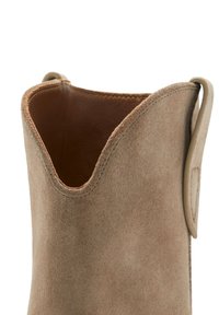 Beige Wildleder-Stiefelette mit V-förmiger Öffnung, glattem Lederfutter und einer kleinen seitlichen Schlaufe für einfaches Anziehen. Strukturiertes Äußeres.
