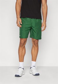 Shorts de sport verts en tissu léger, avec une taille élastique et un petit logo sur le bas à gauche.