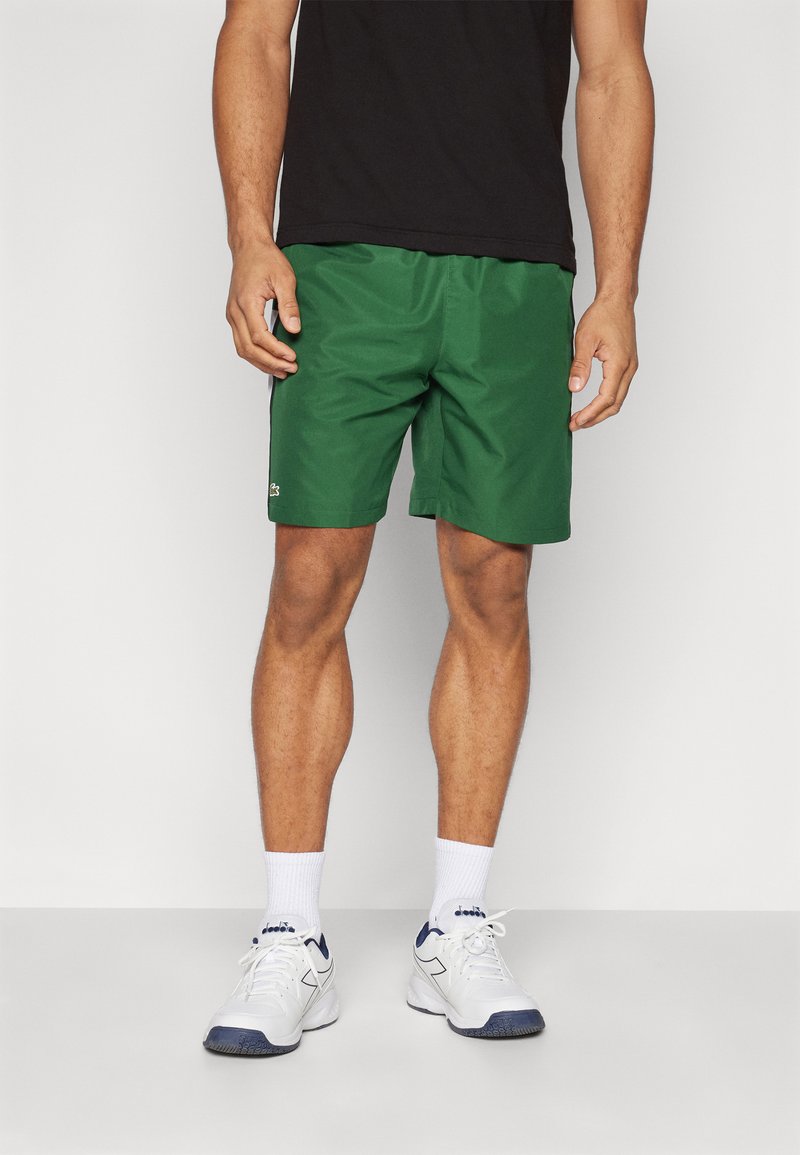 Shorts de sport verts en tissu léger, avec une taille élastique et un petit logo sur le bas à gauche.