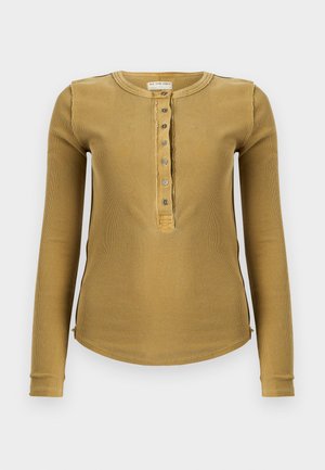 Μπλούζα μακρυμάνικη σε μουσταρδί ριμπ ύφανση με στρογγυλή λαιμόκοψη, κουμπιά μπροστά και πλαϊνές ανοίγματα στο τελείωμα για μεγαλύτερη άνεση στην κίνηση.