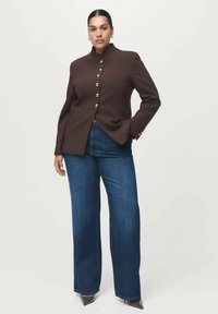 Blazer marrón ajustado con cuello alto y botones plateados, combinado con jeans de mezclilla azul de pierna ancha y tacones negros de punta.