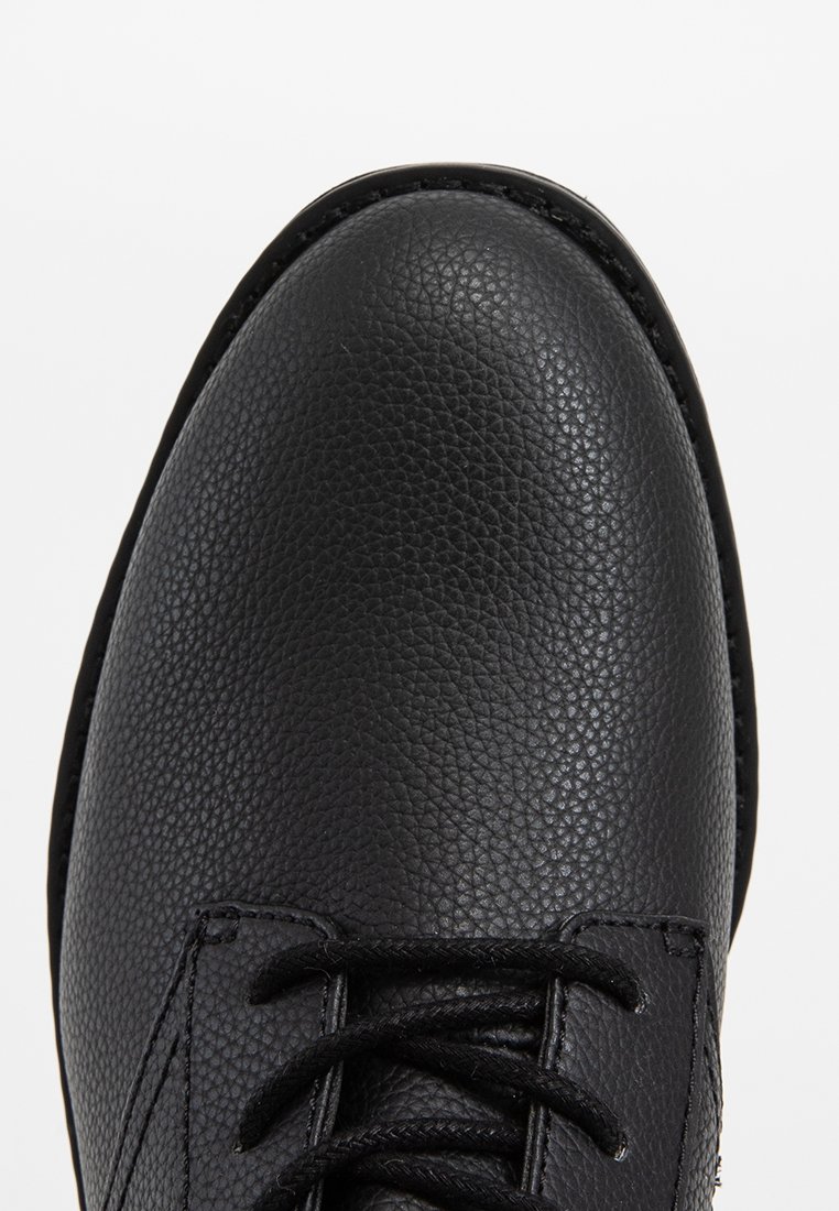 Schwarze Lederschuhe mit einer strukturierten Oberseite, runder Spitze und flachen Schnürsenkeln. Merkmale sind dezente Nähte und eine glatte Gummisohle.