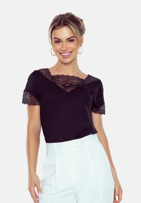 Czarna koszulka z koronkowymi akcentami na rękawach i dekolcie. Krótkie rękawy, dekolt w kształcie litery V, w połączeniu z białymi spodniami o wysokim stanie. Miękka tkanina.