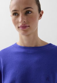 Paarse katoenen sweatshirt met een wijde halslijn en ribgebreide accenten. Bedekt met een klein logodetail op de borst, met een gladde textuur.