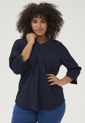 Blouse texturée bleu marine à manches trois quarts, avec un décolleté en V subtil, coupe décontractée et un drapé sur le côté.