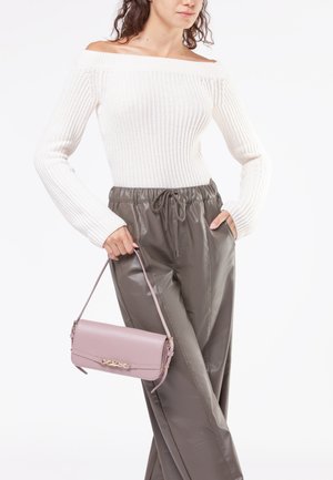 Maglione bianco a coste con scollo a spalle scoperte abbinato a pantaloni elasticizzati verde oliva lucido. Piccola borsa rosa con hardware dorato.