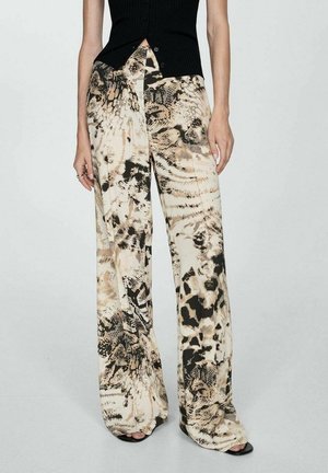 Frau trägt hoch taillierte, weit geschnittene Hosen mit beigem und schwarzem abstraktem Tierdruck, kombiniert mit einem schwarzen ärmellosen Oberteil.
