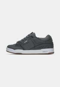 Grijze sneaker van leerachtig materiaal, met een witte tussenzool en een gumrubberen buitenzool. Kenmerkt zich door een ronde neus, een gewatteerde kraag en geribbelde accenten.