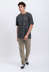 Grijze katoenen t-shirt met een kleurrijk abstract lijnontwerp. Gepaard met lichtbeige broeken en zwarte sneakers met witte zolen en veters.