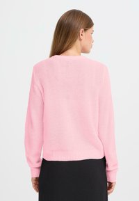 Rosa stickad tröja med texturerad finish, rund hals, långa ärmar och ribbade muddar. Kort design, visad från baksidan.