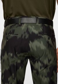 Kamouflagebyxor i nyanser av grönt och svart, med ett elegant svart bälte, två bakfickor och ett slätt, strukturerat tyg.