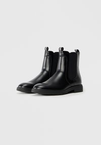 Botas Chelsea negras de piel con paneles laterales elásticos, punta redondeada y tiradores texturizados. Cuentan con una suela de goma gruesa para mayor durabilidad.