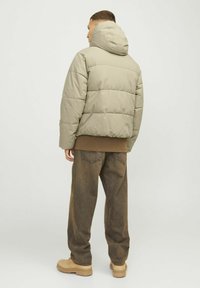 Doudoune couleur vert olive clair, dotée d'une capuche, d'un design matelassé et d'une coupe décontractée, associée à un pantalon ample marron et des bottes beiges.