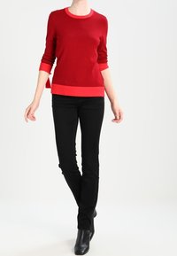 Suéter de punto rojo con cuello redondo y dobladillo en contraste. Combinado con pantalones negros ajustados y botas negras de tobillo. Textura suave en todo.