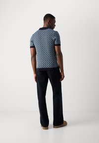 Granatowa koszulka polo z geometrycznym wzorem, z krótkim rękawem i czarnym kołnierzykiem. W połączeniu z ciemnymi spodniami i beżowymi butami.