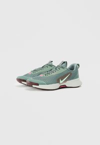 Baskets de sport avec une tige en mesh vert et des accents marron, une semelle blanche et des détails roses. Comprend un swoosh signature sur le côté.
