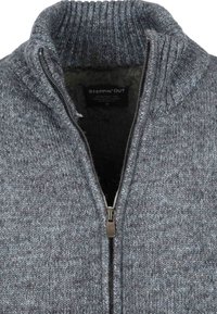 Grijze gebreide trui met een hoge kraag, ritssluiting aan de voorkant en een gestructureerde stof. Binnenkant heeft een zachte voering. Label met de tekst "STEPPIN' OUT."