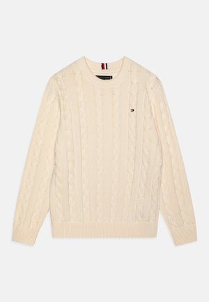 Kremfarget cable-knit genser med rund hals, ribbestrikkede mansjetter og hem. Har en liten logo på brystet. Myk strikket tekstur.