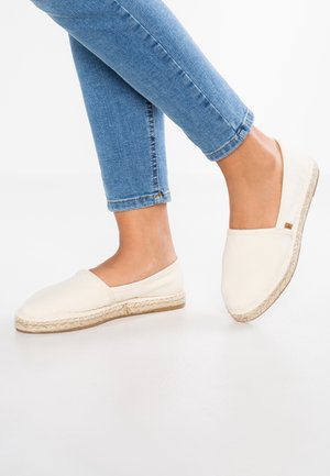 Fødder iført hvide lærredsesspadriller med jutesåler, kombineret med blå skinny jeans, mod en ensartet hvid baggrund.