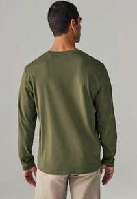 Langärmliges Shirt aus dunkelgrünem Baumwollstoff. Merkmale einen klassischen Rundhalsausschnitt, enganliegende Ärmel und eine glatte Textur. Keine sichtbaren Logos oder Muster.