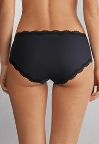 Black lace-trimmed underwear with a smooth texture, featuring a scalloped edge, designed for comfort and coverage.