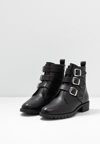 Svarta läderankelstövlar med tre justerbara remmar som har silverfästen och nitar. Rund tå, låg klack, texturerad sula.