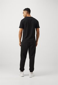 Mustat t-paita ja siihen sopivat verkkosaat, jotka on valmistettu pehmeästä kankaasta. Niissä on rento istuvuus ja joustavat hihan suut. Yhdistetty valkoisiin urheilukenkiin.