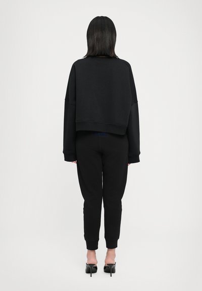 Black cropped sweatshirt and black joggers, both made of a soft fabric. The joggers feature ribbed cuffs. Black high-heeled shoes.