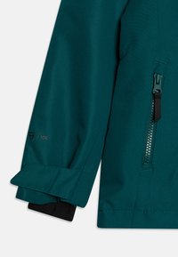 Ärmens detaljer på den teal jackan har ett texturerat tyg med en ficka med dragkedja och logodetalj; inkluderar kontrasterande svart manschettfoder.