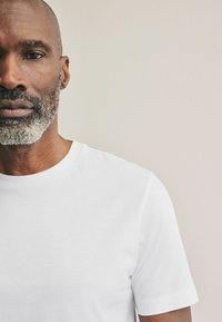 Weißes Baumwoll-T-Shirt mit rundem Halsausschnitt und kurzen Ärmeln, glatte Textur und minimalistisches Design. Keine sichtbaren Muster oder Akzente.