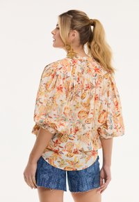 Blouse à manches bouffantes avec un motif floral en orange, jaune et bleu sur un fond clair, accompagnée de shorts en denim.
