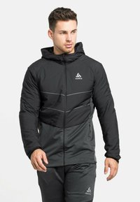 Schwarze und graue isolierte Jacke mit Kapuze, mit einem Reißverschluss, reflektierenden Akzenten und strukturierten unteren Panelen.