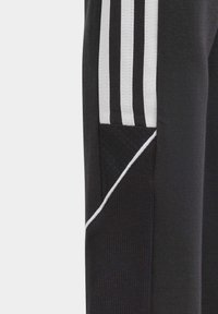Pantalons de sport noirs avec des rayures blanches, un tissu texturé, un design fuselé et des accents de panneaux contrastants. Comprend une pochette latérale.