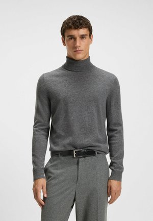 Un pull à col roulé gris en matière douce, avec des manches longues et des poignets côtelés, associé à un pantalon gris et une ceinture noire.