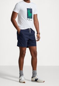 Vit bomull T-shirt med en grön polo spelare grafik, parat med marinblå shorts, grå strumpor och vita sneakers med blå detaljer.