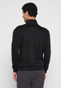 Zwarte sweatshirty met een hoge kraag en geribbelde manchetten en zoom. Gemaakt van een gestructureerde stof, heeft een losse pasvorm en een minimalistisch ontwerp.