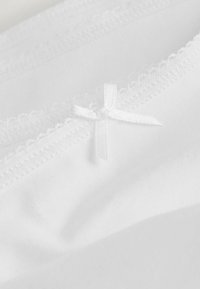 Witte katoenstof met een delicate kantafwerking en een klein wit strikje met een textuurfinish. Zachte en gladde uitstraling.