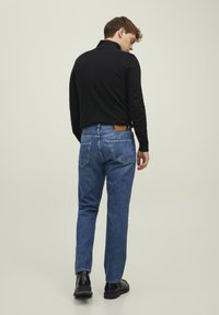 Svart langermet polo, blå denim jeans, slim fit. Jeansene har to baklommer og en beigefarget lærlabel i livet. Svart støvler.